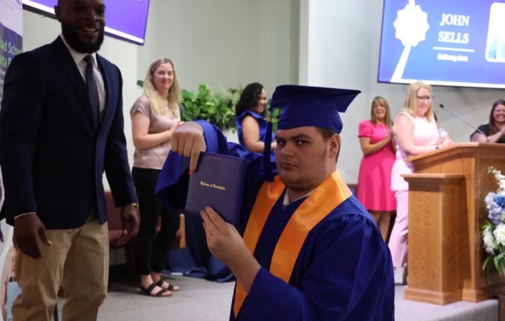 Carl Blackmon stands beside a High Road School of Santa Rosa student in a graduation cap and gown holding a diploma.