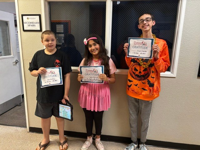 Tres alumnos de la Sierra School de Gilbert exhiben los premios «Character Strong Gratitude» en el pasillo del colegio.