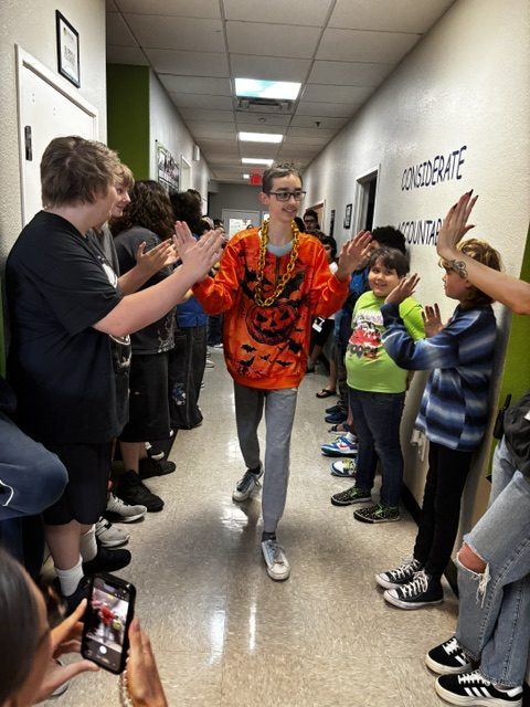 Un alumno de la Sierra School de Gilbert, vestido con una camiseta naranja, atraviesa el Victory Tunnel mientras sus compañeros le animan.