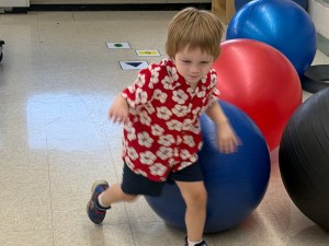 Young student participating in a movement activity with a therapy ball in the early childhood classroom.