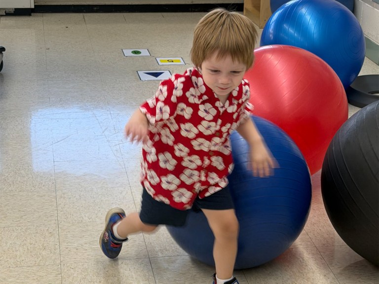 Young student participating in a movement activity with a therapy ball in the early childhood classroom.
