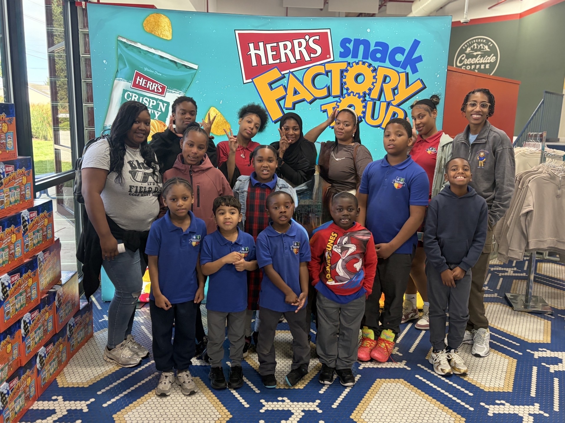High Road School at Chester Community Charter School students pose outside the Herr’s factory beside a large red wall displaying the company logo.