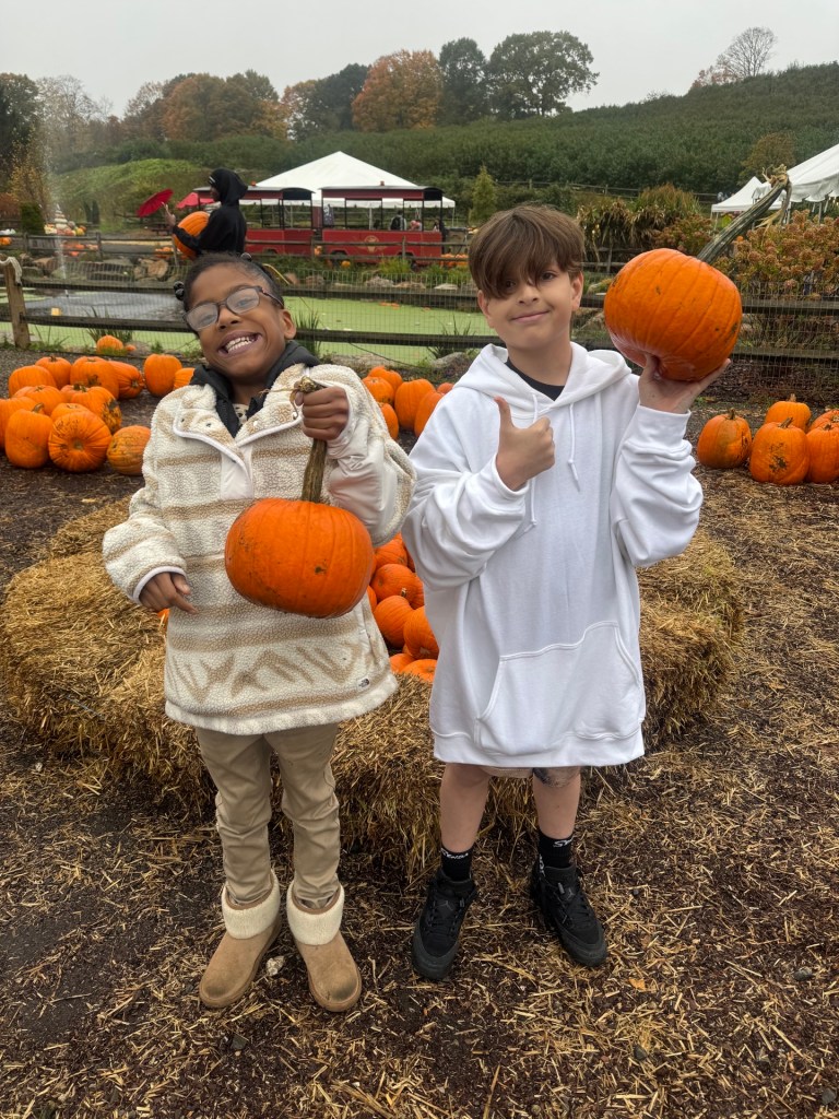 Dos alumnos de la escuela High Road del condado de Fairfield sonríen mientras sostienen las calabazas que han elegido durante su excursión a la granja Silverman's Farm.