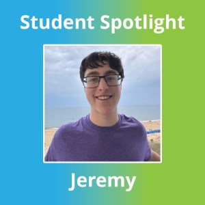 Jeremy sonríe con las gafas puestas y una camiseta morada, con el mar y la playa a sus espaldas.