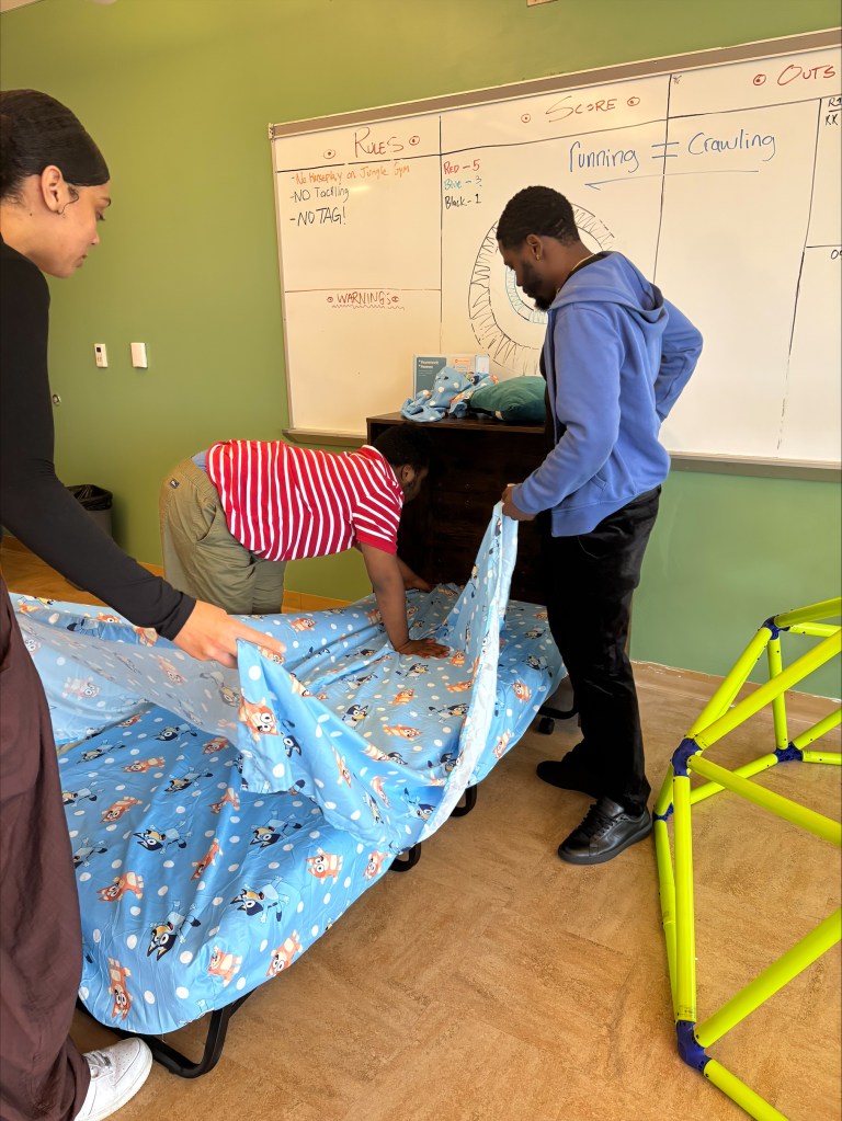 A student practices making a bed with staff support in the Bloom classroom at High Road School of Delaware.