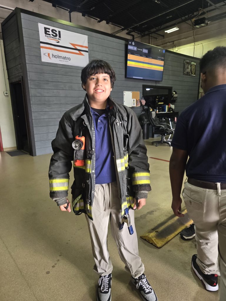 Un alumno lleva un casco de bombero junior de Alliance Fire Rescue durante la visita a la estación.