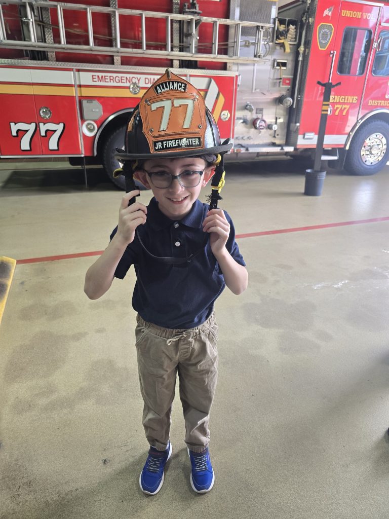 Un alumno lleva un casco de bombero junior de Alliance Fire Rescue durante la visita a la estación.