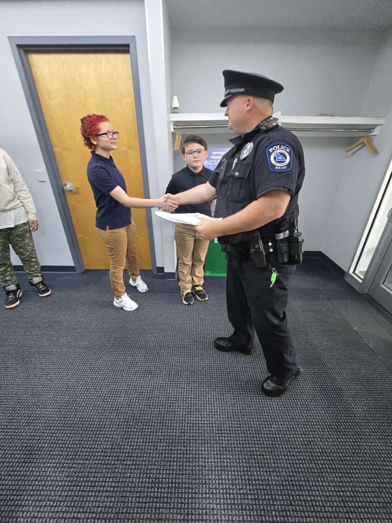 Un alumno de la High Road School de York estrecha la mano a un agente de la Policía Regional del condado de York mientras le entrega una carta de agradecimiento.