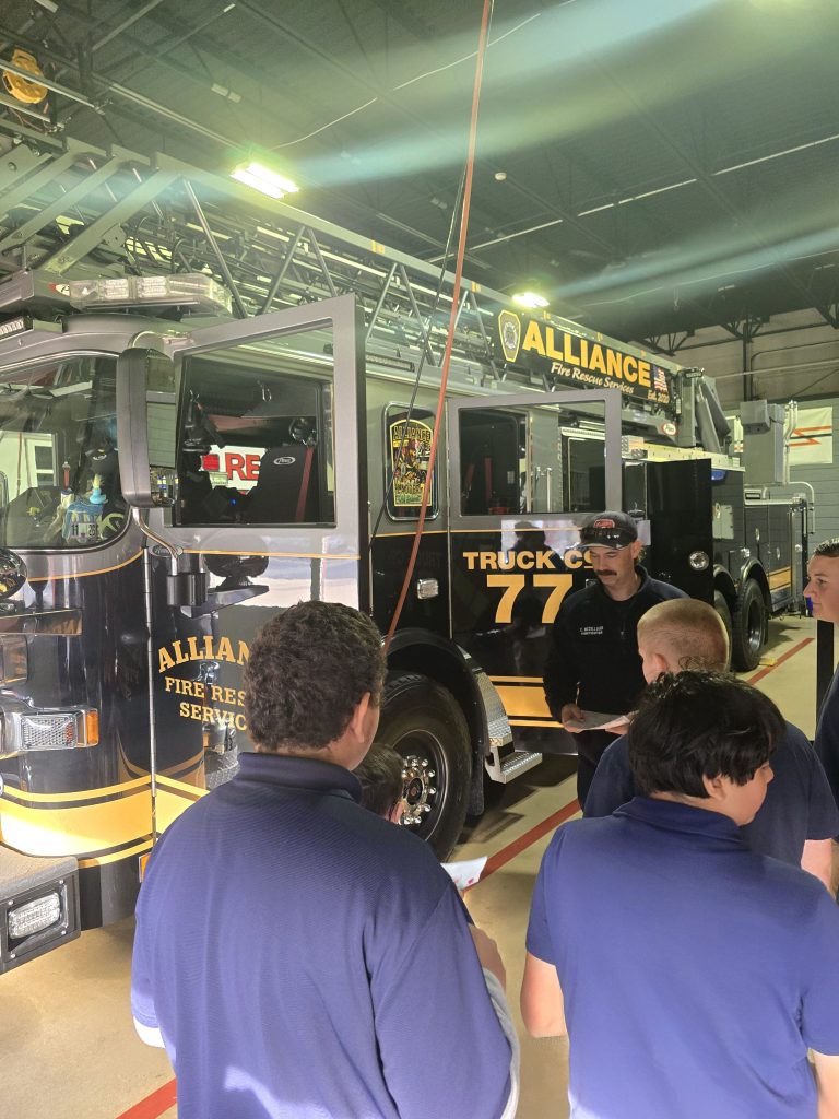 Los alumnos aprenden sobre el equipamiento de extinción de incendios durante una visita al cuerpo de bomberos de Alliance.