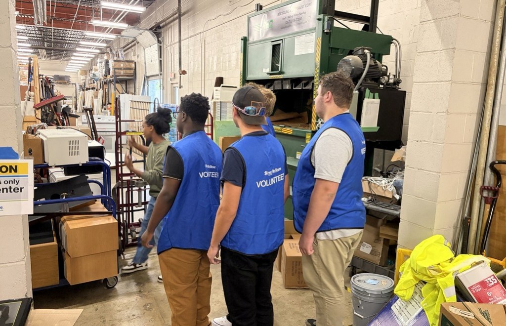 High Road School of Nashville students wearing blue volunteer vests stand near industrial equipment at Habitat for Humanity ReStore.