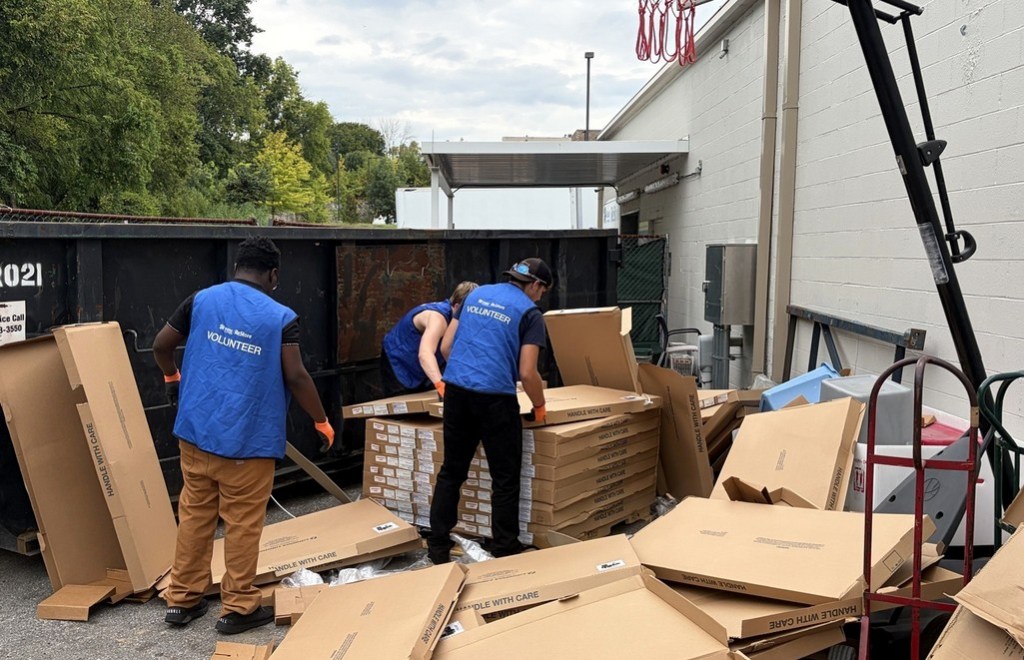 High Road School of Nashville students wearing volunteer vests handle cardboard near an outdoor dumpster at Habitat for Humanity ReStore.