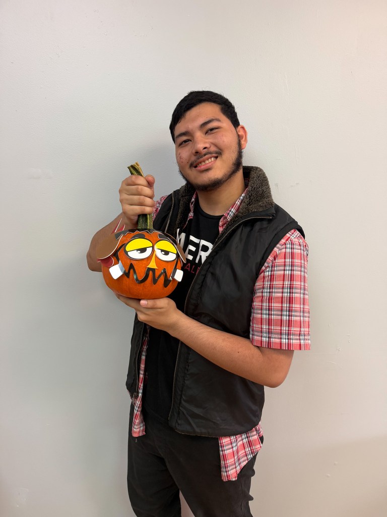 High Road School of Hoffman Estates Fall Fest participant wearing a plaid shirt and black vest smiles while holding a decorated pumpkin.