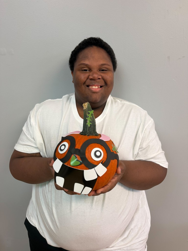 Smiling Fall Fest participant at High Road School of Hoffman Estates holds a pumpkin decorated with oversized eyes and a toothy monster face.