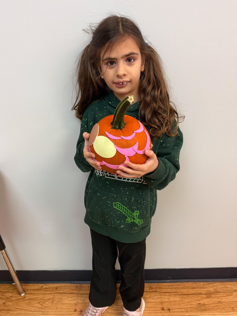 High Road School of Hoffman Estates student wearing a green sweatshirt displays a pumpkin decorated with colorful paper facial features.