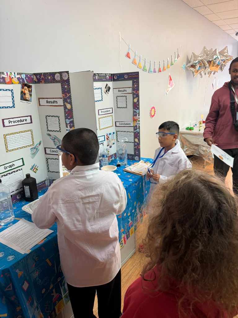 Los alumnos de la High Road School de Hoffman Estates, ataviados con batas blancas de laboratorio y gafas de seguridad, presentan sus experimentos en la feria de ciencias del colegio.