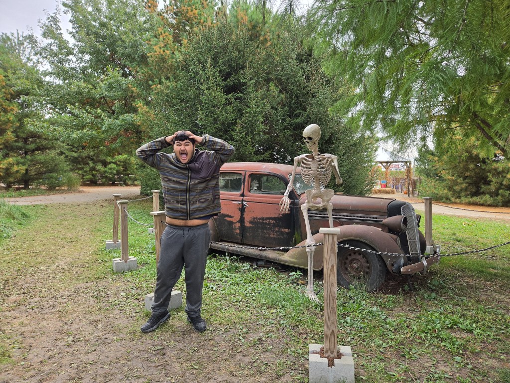 Un estudiante posa junto a un coche clásico y una decoración con forma de esqueleto en Lincoln Ridge Farm.