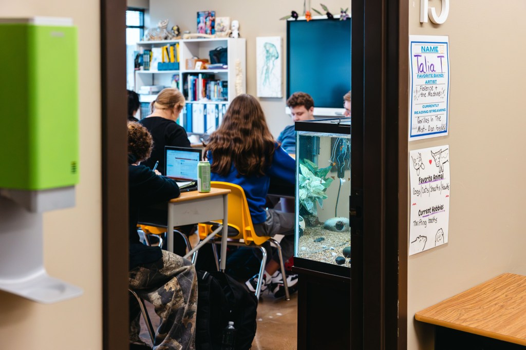 Los alumnos trabajan juntos en un aula de la NewHope Academy con ordenadores portátiles, material escolar y un acuario en el aula.