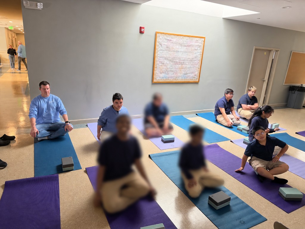 Students and staff at High Road School of Anne Arundel County sit on yoga mats while participating in a guided yoga session.