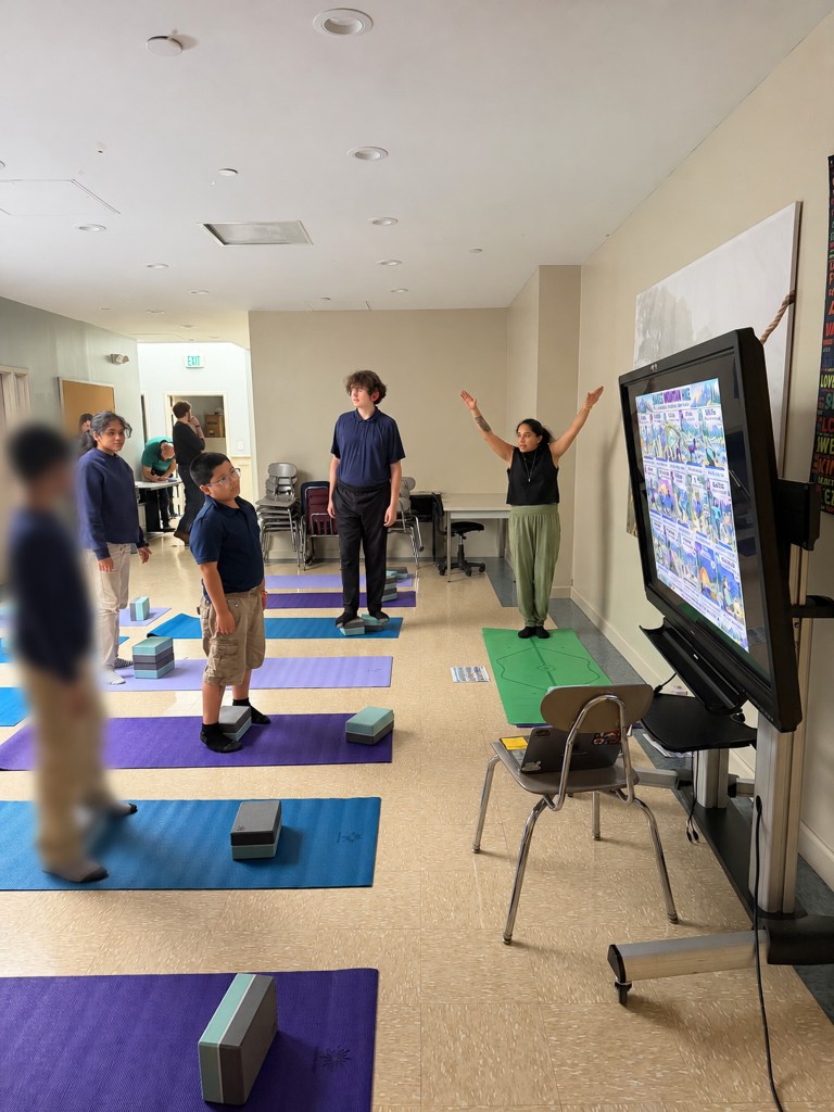 Students follow along as Program Director Tara Chander leads a standing yoga pose during a Friday wellness session.