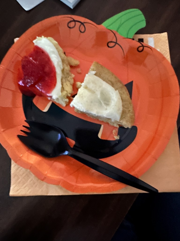 Pumpkin-shaped plate with a partially eaten cookie and black utensils during the Pick-Me-Up Cart staff treat event.
