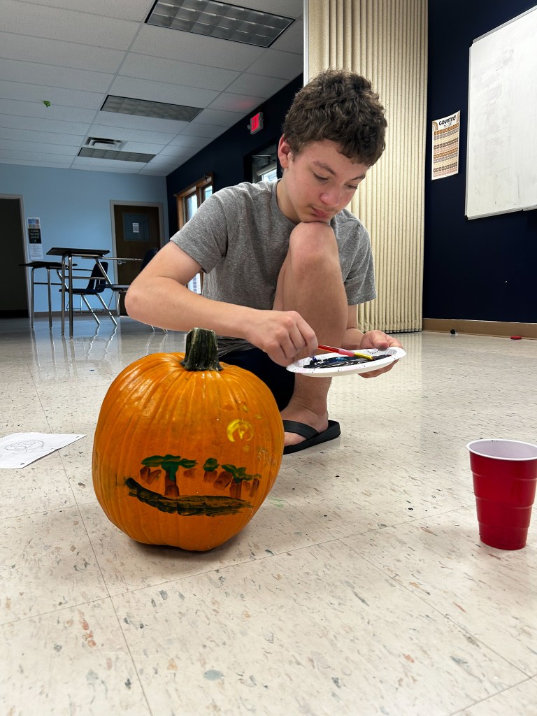 Un alumno muestra una calabaza pintada de colores en la escuela High Road School del condado de Cole.