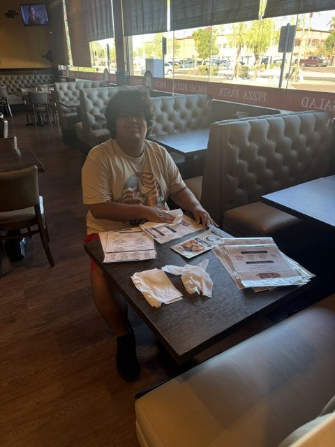 Sierra School of Gilbert student reviews restaurant menus at a table inside Sal's Gilbert Pizza.