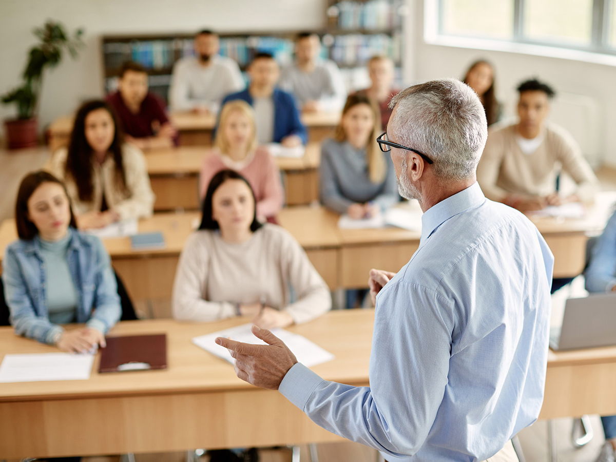 Un ponente imparte una sesión de formación profesional a un grupo de adultos sentados en un aula.