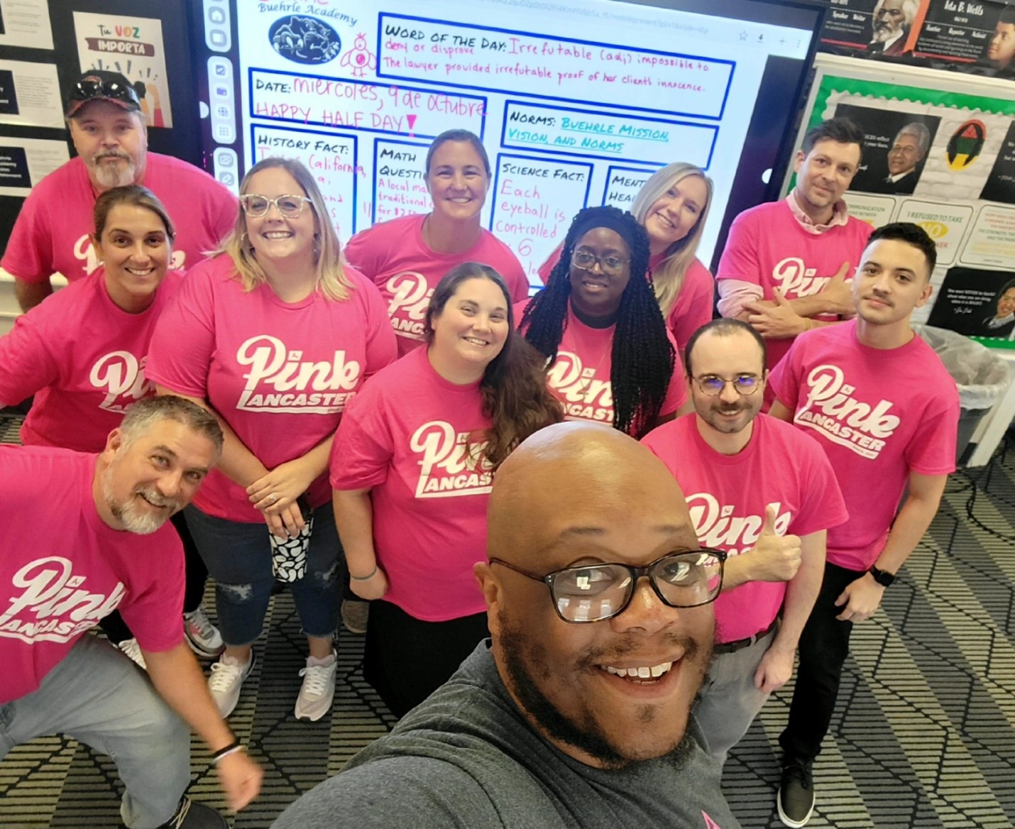 Buehrle Academy staff selfie featuring: Larry Lewis, director of operations; Joel Bacharach, executive director; Jennifer Sumrall, administrative assistant; Bill Brothers, building engineer; Kristen Renzi, career development; Bethany Kyper, teacher of personal development; Andrea Brown, CA teacher; Leisa Ezibe, math teacher; Erin Haggard, director of student services; Michael Falcone, social studies teacher; Jermaine Rivera, behavioral specialist; and Jason Krapf, science teacher.